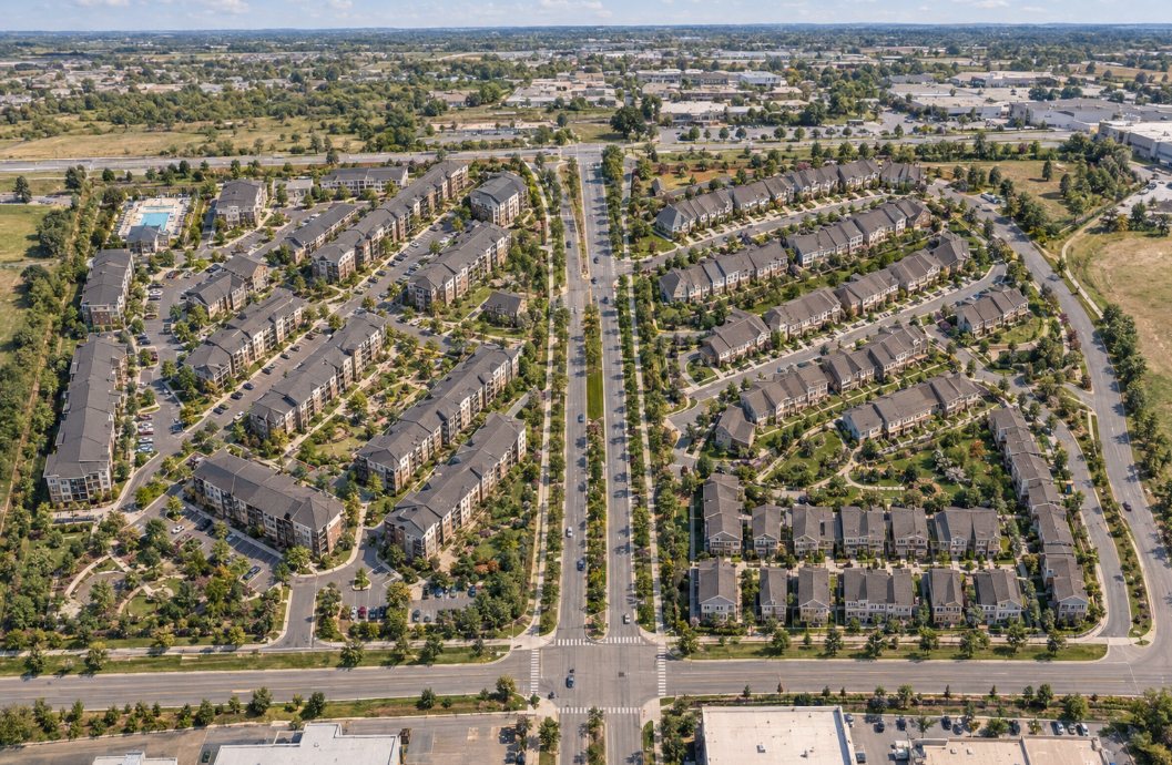 Aerial view of a garden apartment and townhome community with a central boulevard, pool, and tree-lined streets